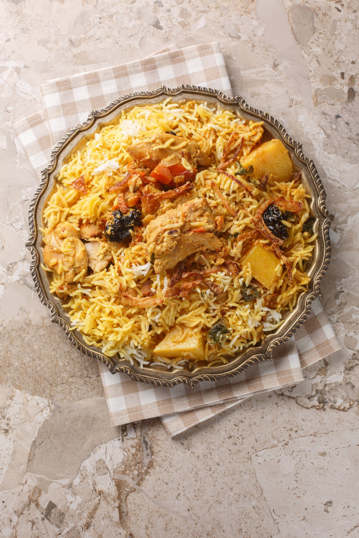 Sindhi biryani with rice, chicken, potato, tomato, prune, mint, lemon and coriander closeup on the plate on the table. Vertical top view from above