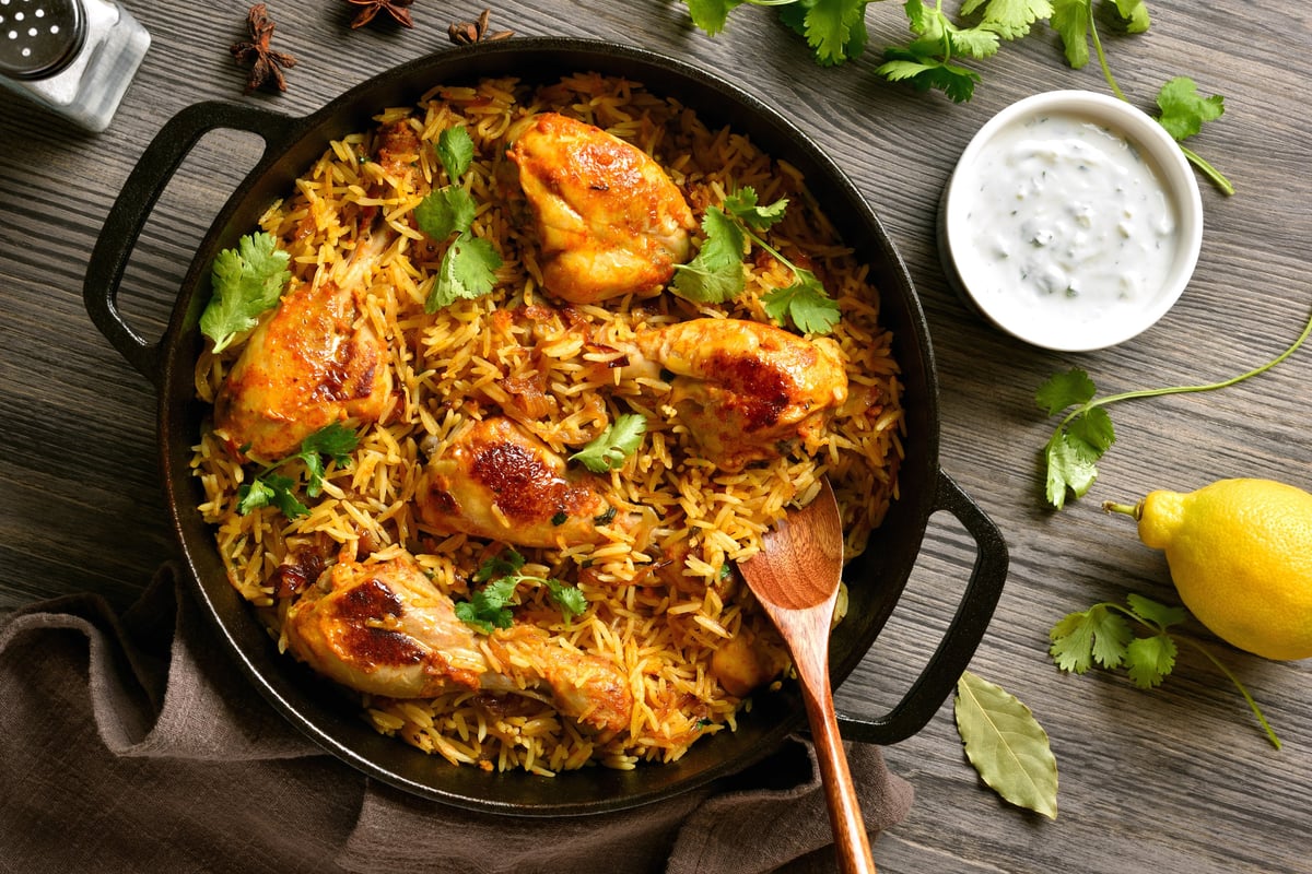 Homemade delicious chicken biriyani served in cast iron pan on dark wooden background. Traditional indian dish. Top view, flat lay
