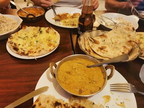 Indian meal spread with naan bread, curries, and flatbreads on wooden table with diners