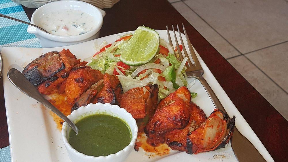 Tandoori chicken pieces on a white plate with green chutney, coleslaw, lime wedge, and white sauce on the side