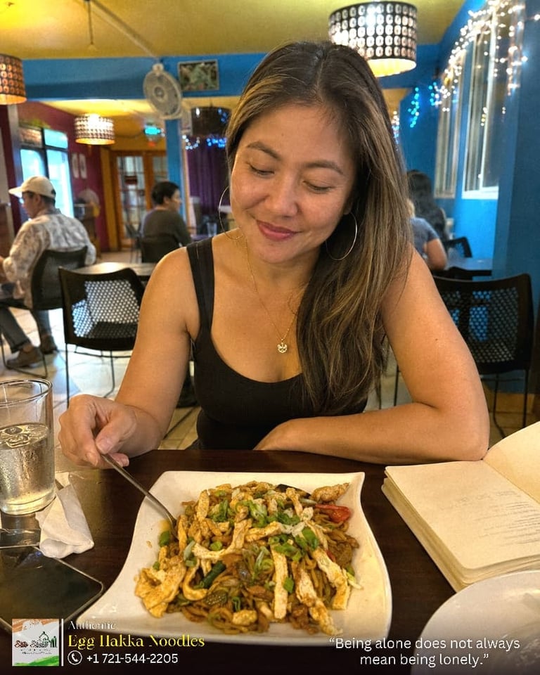 Woman smiling while eating egg hakka noodles at a restaurant with colorful blue and yellow decor