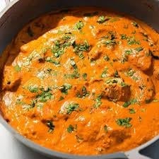Creamy tomato-based curry with chicken and fresh basil garnish in a dark pot