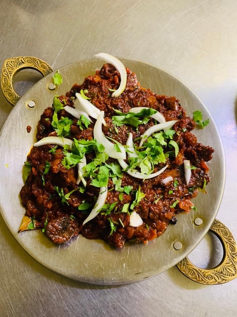 Beef curry dish with sliced onions and fresh cilantro garnish served in a decorative brass-handled bowl