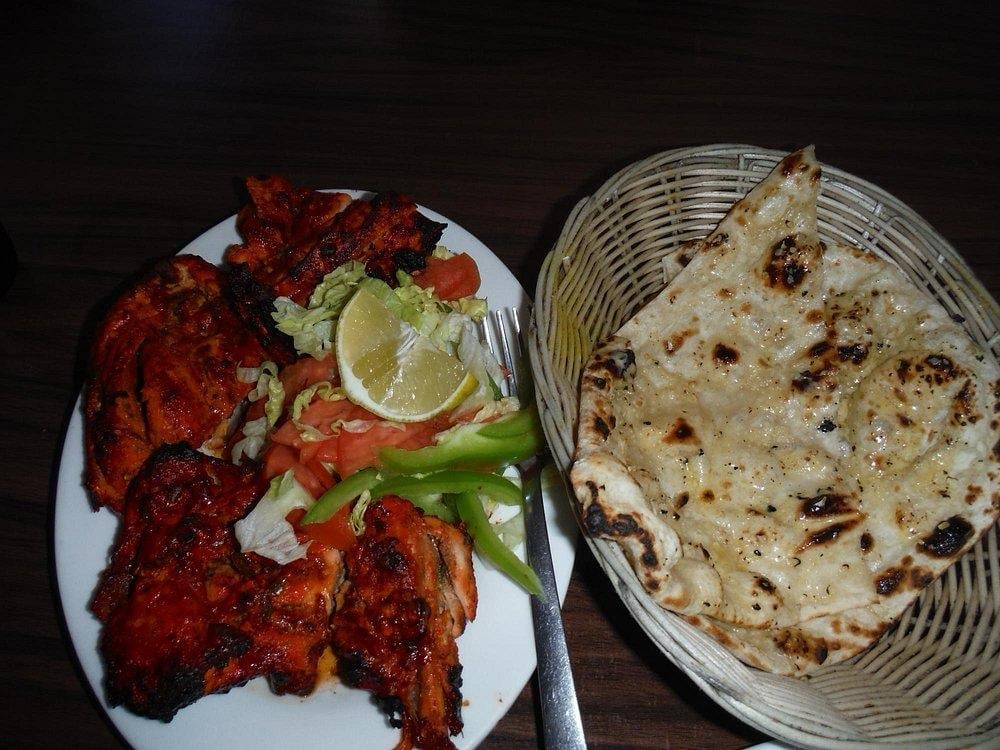 Grilled tandoori chicken on a white plate with lemon and peppers, served with roti bread in a basket