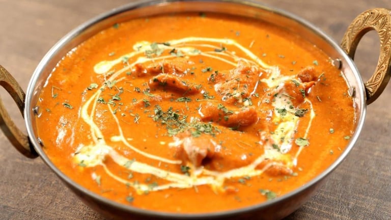 Creamy tomato curry in a metal bowl with cream swirl, topped with meat pieces and herbs