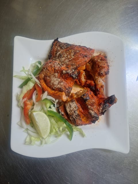 Grilled chicken with red rub on white plate with fresh lime, cucumber, and red pepper garnish