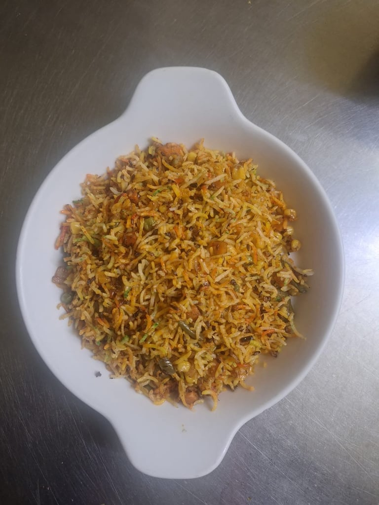 Golden crispy fried onions piled in a white ornate serving dish on a metallic surface