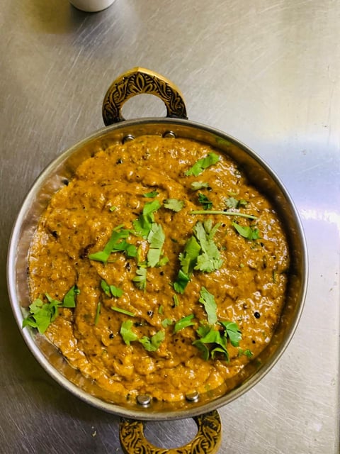 Indian curry dish in brass cooking vessel garnished with fresh cilantro leaves